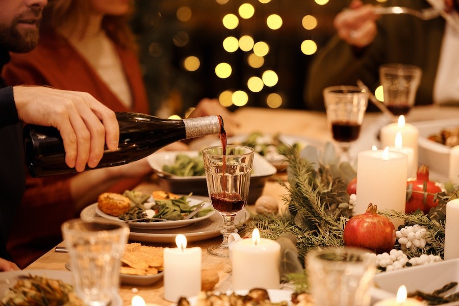 Host pouring wine in a glass at a holiday dinner table. 