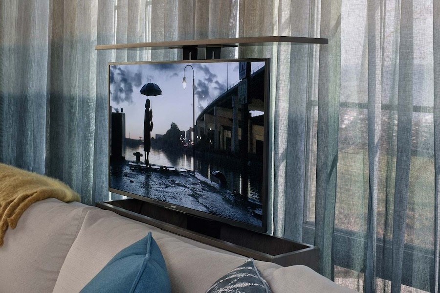 motorized TV lift in the raised position behind a couch. Sheer curtains are in the background.