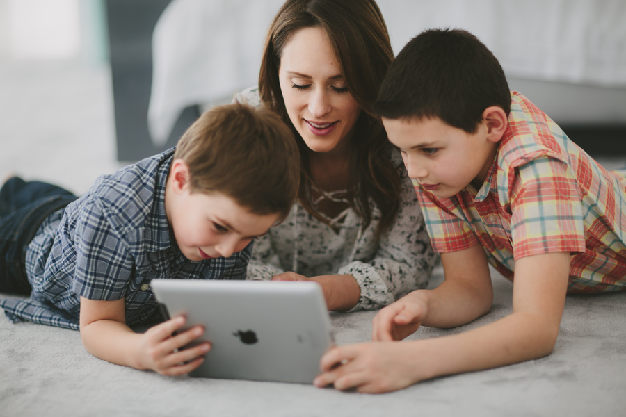 A mother and her two children watching something on an iPad while lying on the floor.