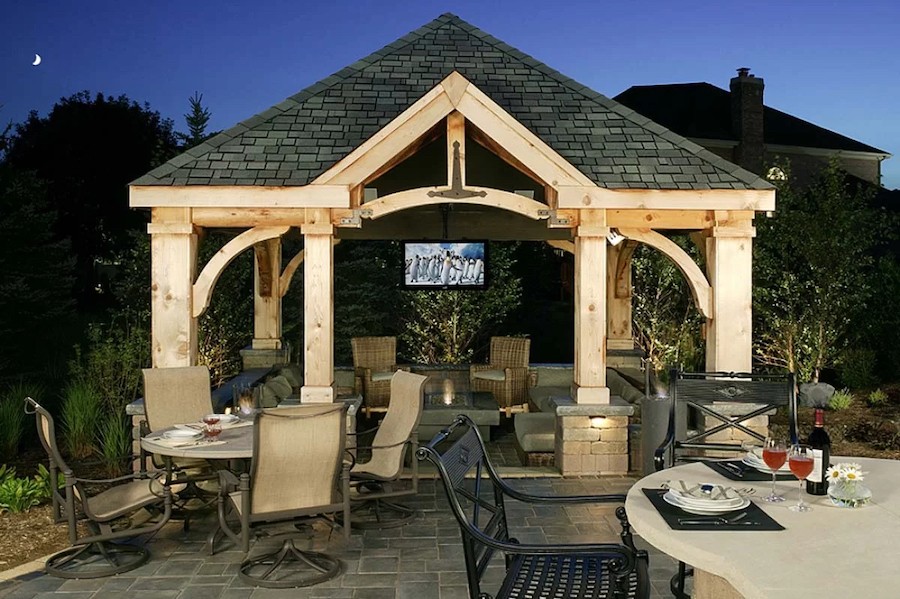 An outdoor space with a dinner party in the late evening. An outdoor TV is installed under a porch roof.