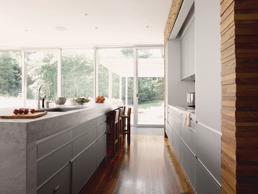 Ultra-modern kitchen with sleekly integrated automation technology overlooking a green view with large glass windows and doors.